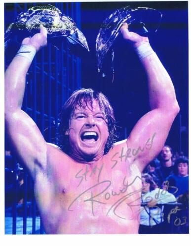 ROWDY RODDY: A colour picture of Rowdy Roddy Piper, holding two belts. Autographed