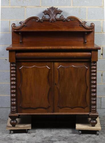 CHIFFONIER: A late 19th century carved Australian cedar chiffonier, raised on bun feet, the doors flanked by bobbin turned half pilasters and the having a carved pelmet with scrolling gallery above a single shelf, 144cm high, 110cm wide, 47cm deep