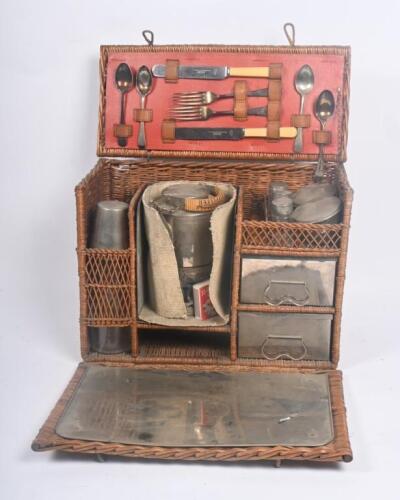 TEA BASKET: An early travel tea hamper set, within fold out cane basket, includes lamp and kettle, two cups with glass bottle, two drawers with porcelain inserts and cutlery.