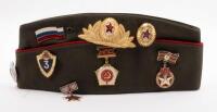 USSR: A Soviet Military styled Garrison hat, green with red piping. Fitted with various Soviet era pins.