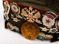 USSR: A Soviet Military styled Garrison hat, green with red piping. Fitted with various Soviet era pins and three patches attached. - 3