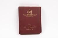REGISTER: A 1979 edition of Aston Martin Owners Club register book within red vinyl binder folder, gold gilt writing to cover. Pages with damage, including water damage and foxing.