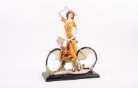SCULPTURE: A resin sculpture of a lady on a bicycle, mounted to timber base, measures 38cm high
