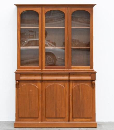15D · BOOK CASE: A two tiered timber bookcase by Pfitzner Furniture South Australia, featuring glazed display cabinetry, with a drawer and storage space to the lower, 137cm wide, 207cm high, 47cm deep
