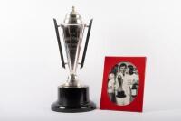 TROPHY: A large two-handled trophy on round bakelite base awarded to Alan Hamilton at the 1976 Daily Mirror Sports Sedan Classic, comes with framed & glazed photograph of Alan Hamilton holding said trophy whilst being kissed by two grid girls