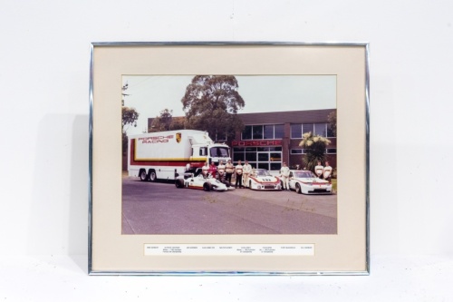 PORSCHE RACING: A large framed & glazed photograph, taken circa early 1980s of the Porsche Racing Team featuring the various Porsche racing cars, Alan Hamilton, Alfredo Costanzo, Alan Jones, Colin Bond & support staff