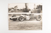 DENIS HULME: A large original black & white photograph by Lawrence Thomas of Dennis Hulme racing a BT19, signed by Dennis Hulme 'With Very Best Wishes - Dennis Hulme', 49cm high, 59cm wide