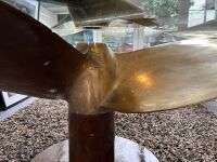 PROPELLOR: A large decorative solid brass ships propellor mounted on timber base, under circular bevel cut glass table top - 6