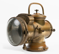HEADLIGHT: A circa early 1900s Herm Riemann (Germany) brass headlight, convex lens width 18cm (7 inches), vertical bail handle, overall height 34cm [Location: Melbourne]