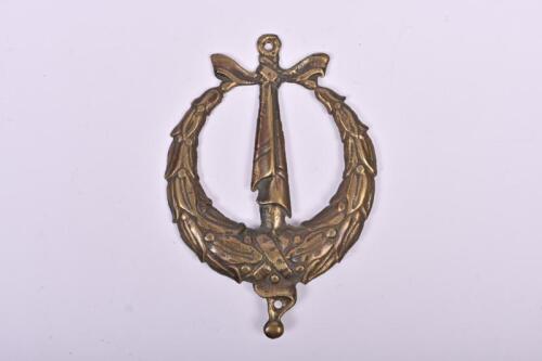 MILITARY: A brass car badge depicting wreath with sword and sheath