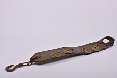 HORSE BRASSES: A set of vintage horse brasses on leather strap, one end fitted with a heavy cast iron hook, 97cm long