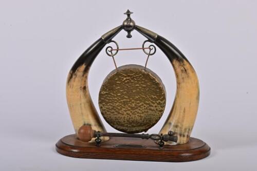 DINNER GONG: An Edwardian Scottish cow horn dinner gong, two cow horns mounted on carved English oak with brass gong hanging by leather straps, 30cm high