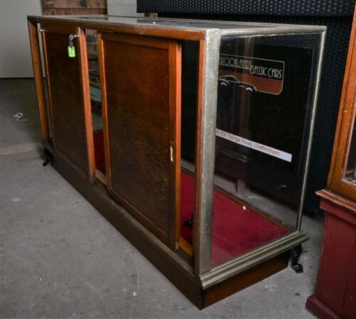 DISPLAY CABINET: An early 20th century metal and glass mirror back counter display cabinet bu Boston Co, Melbourne, the rear with three sliding oak doors with locks and key, cast iron feet, 98cm high, 184cm wide, 55cm deep