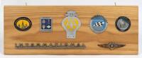GRILLE BADGES: A collection of car grille badges mounted on a pine backboard, including an enamelled Victorian Sporting Car Club badge, a Briggs Cunningham Automotive Badge and a 1960-61 AA membership badge, the board 24 x 66cm