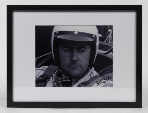 BRABHAM: A signed photograph featuring Sir Jack in his Brabham, likely BT19 of 1966, mounted and framed, 19.5cm high x 24cm wide.