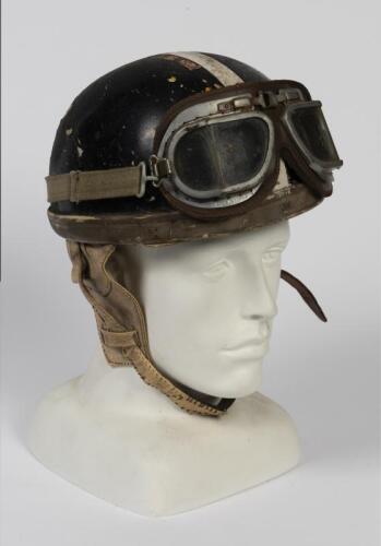 PLUM PUDDING HELMET: A vintage pudding basin motorcycle helmet a pair of googles, fitted with canvas straps and a leather ear flaps and chin strap, no maker or size