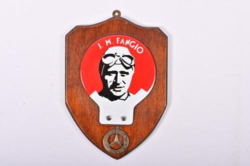 FANGIO: A 'J.M. FANGIO' shield, with applied J.M. Fangio enamel grill badge, with brass 'FANGIO Y CIA S.A - MAR DEL PLATA' (Argentinian city) badge to plaque base.