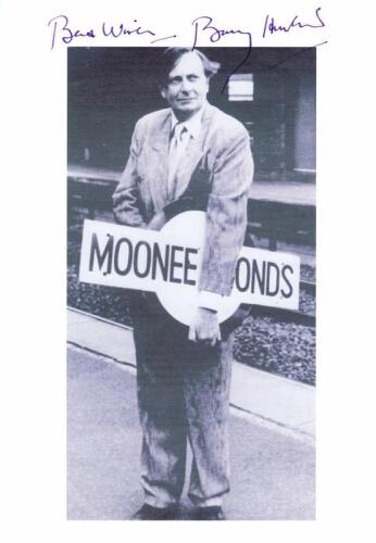 BARRY HUMPHRIES: A black and white picture depicting Barry Humphries holding Moonee Ponds platform sign, autographed "Best Wishes" by Barry Humphries.