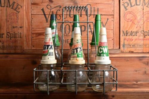 OIL BOTTLE RACK: A vintage wire rack with three five half litre and three litre oil bottles, with circa 1990/2000s Mobil plastic pourers and dust caps